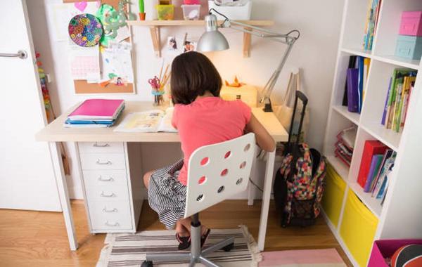 صورة لطفلة تجلس إلى مكتب الدراسة في غرفتها