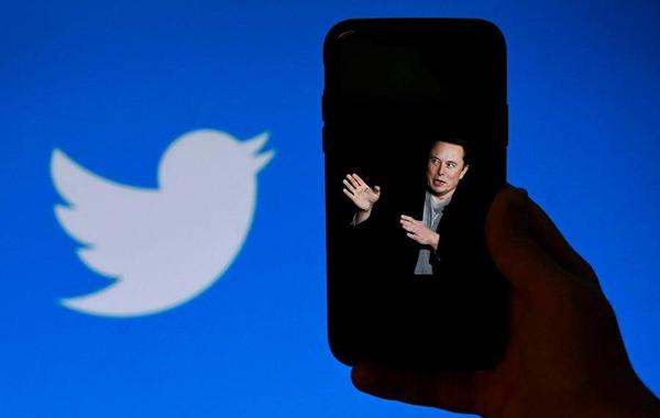 a photo of Elon Musk with the Twitter logo shown in the background, on October 4, 2022, in Washington, DC. Elon Musk has offered to push through with his buyout of Twitter at the original agreed price, reports said Tuesday, prompting a surge in the share price of the social network that triggered a suspension of trading. OLIVIER DOULIERY / AFP